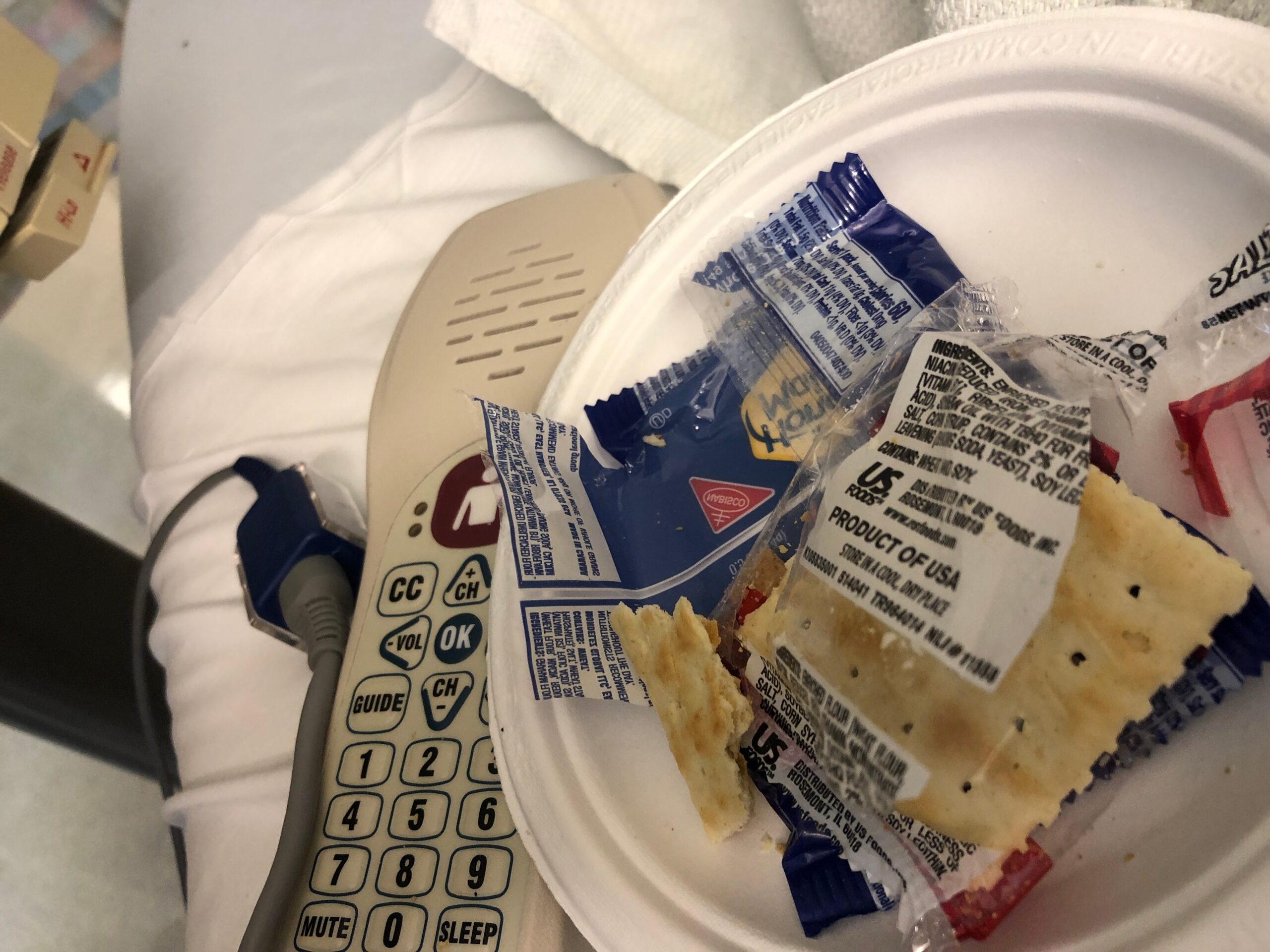 An off-center photo of a hospital bed, with a call device and a paper plate with saltine crackers.