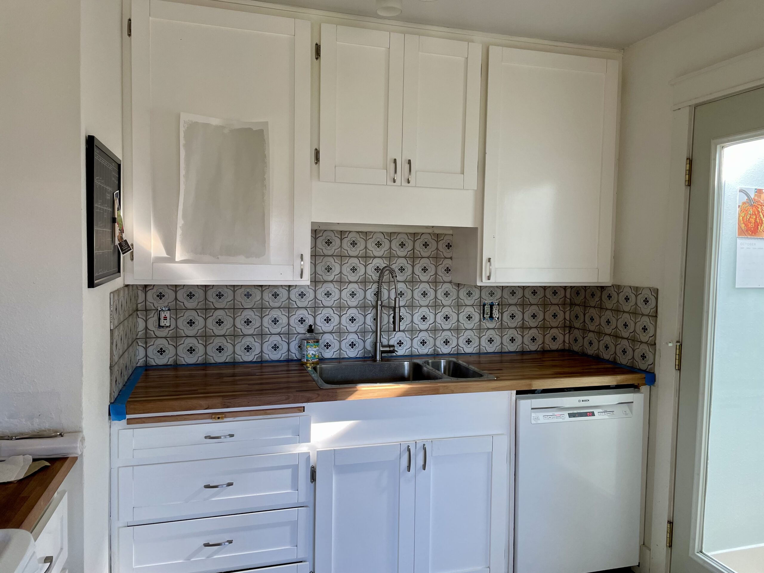 Same view of kitchen, with dark butcher-block counter tops and colorful tile backsplash that fills wall behind sink.