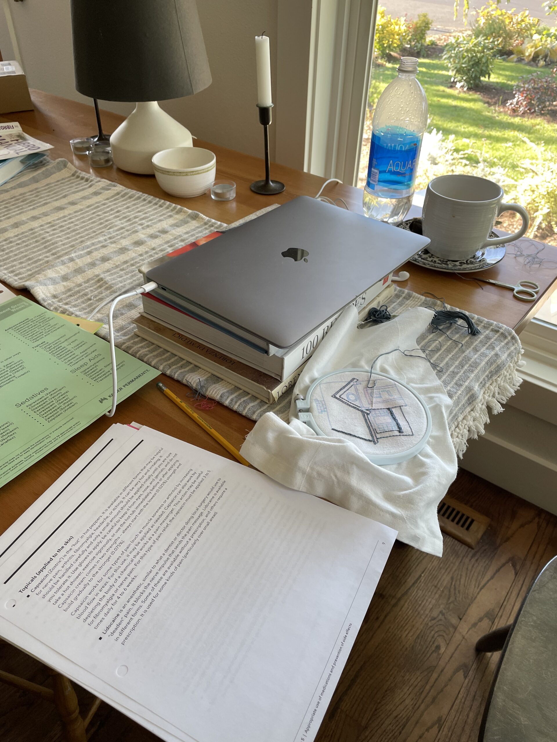 Tabletop with laptop, coffee mug, papers, and needlework.